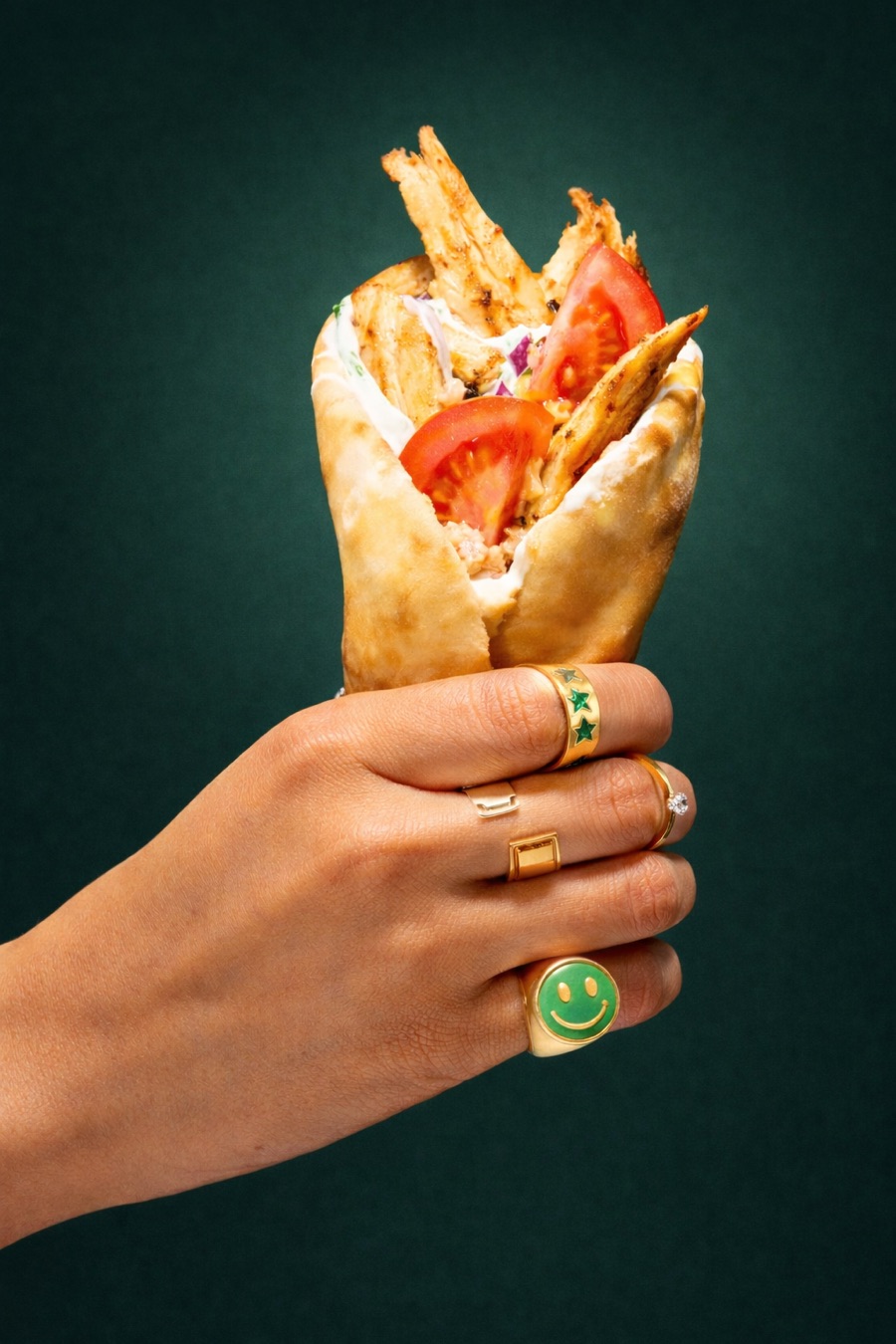 Hand holding an LJ’s Quality Foodz gyros against a green backdrop