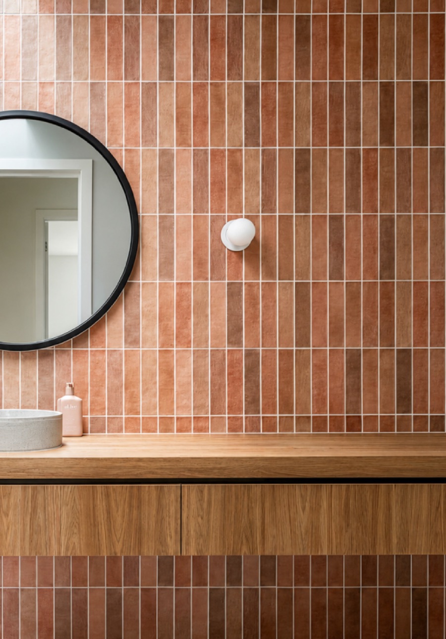 Terracotta tiled bathroom with round mirror and timber vanity