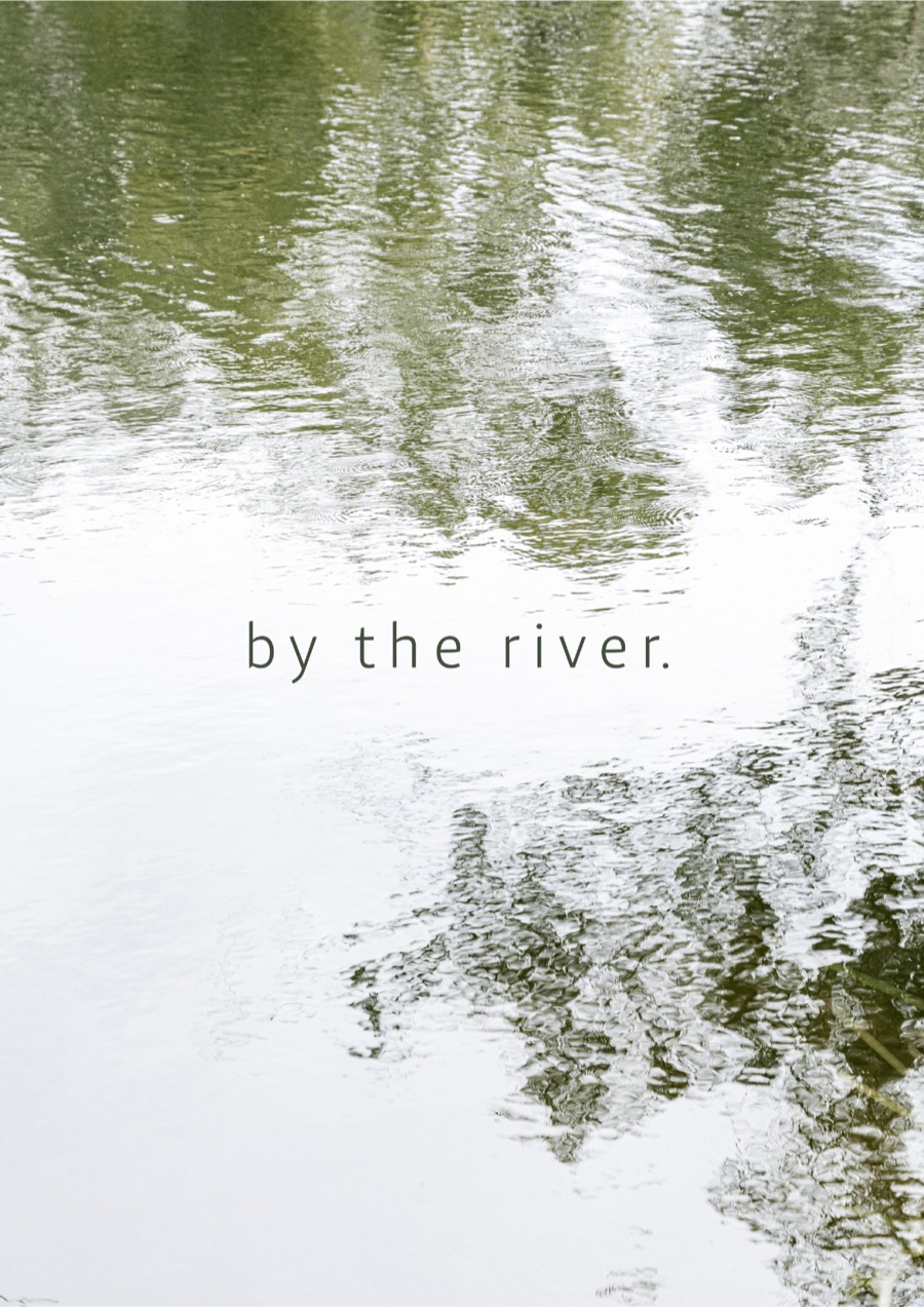 Trees reflected on river water with the words by the river