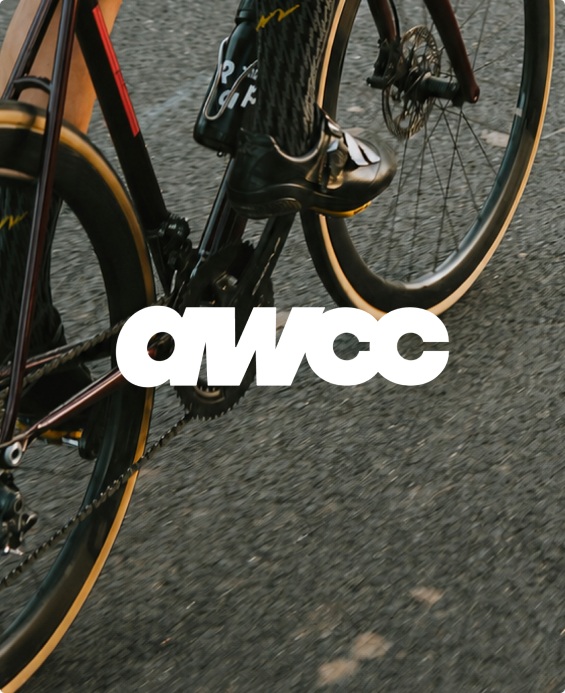 Close-up of a road bike’s cranks and wheels on asphalt, overlaid with the white AWCC wordmark