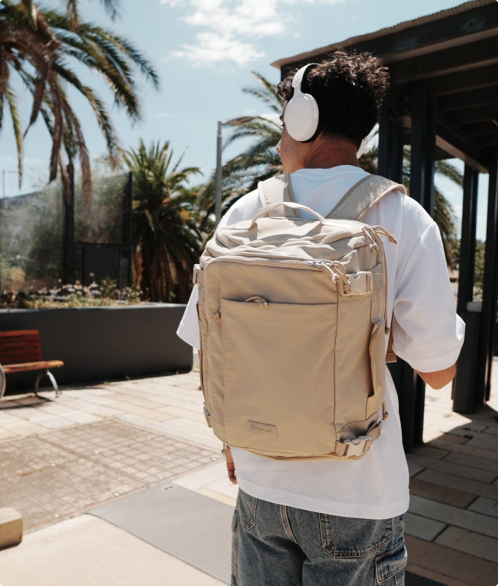 Person seen from behind wearing white headphones and a beige backpack outdoors