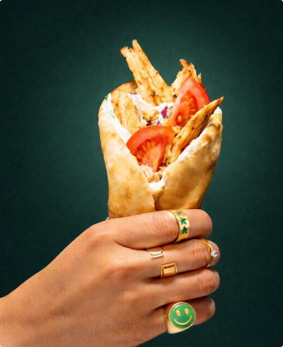 Hand holding a filled gyros wrap against a dark backdrop