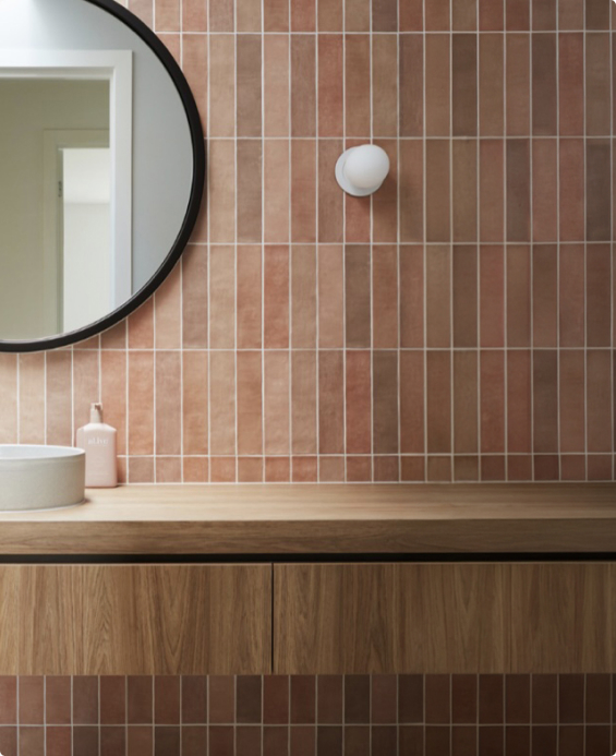 Terracotta-tiled bathroom with a round black-framed mirror above a timber vanity