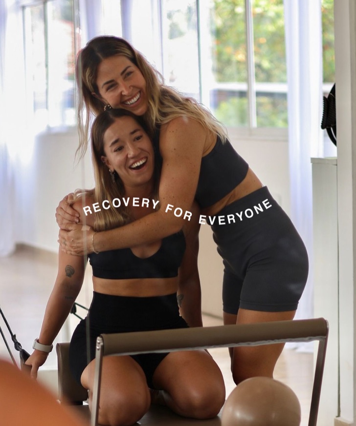 Two women laughing mid-embrace under the line Recovery For Everyone